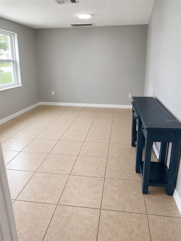 A room with light gray walls, tan tile flooring, a window, and a blue console table — 7325 IVANHOE DRIVE, PORT RICHEY, FL