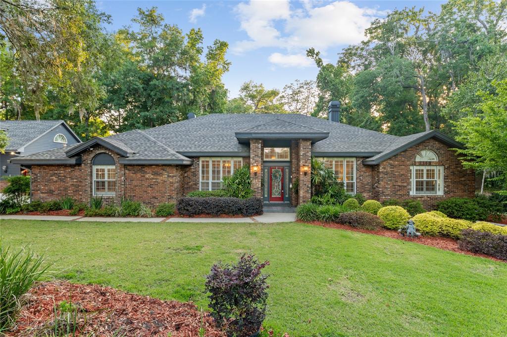 An exterior view of a brick home entrance with a red door and text overlay — 2512 NW 58TH BOULEVARD, GAINESVILLE, FL