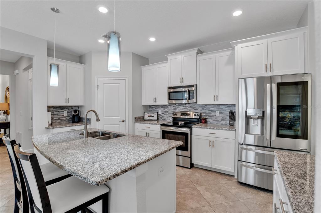 A kitchen features white cabinets, granite countertops, stainless steel appliances, and a central island — 1419 PRO SHOP CT, DAVENPORT, FL