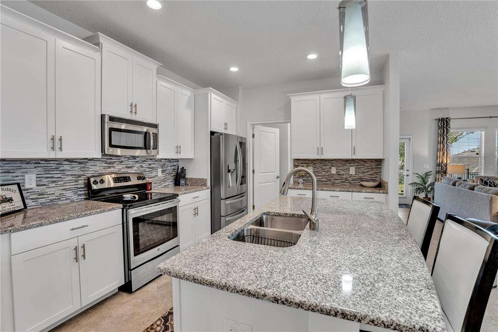A kitchen features white cabinets, granite countertops, a stainless steel island sink, and tile backsplash — 1419 PRO SHOP CT, DAVENPORT, FL