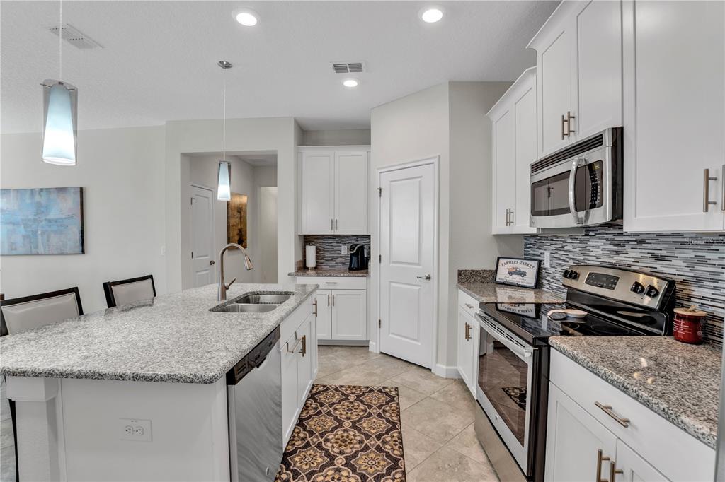 A kitchen features white cabinets, granite countertops, a center island, and stainless steel appliances — 1419 PRO SHOP CT, DAVENPORT, FL