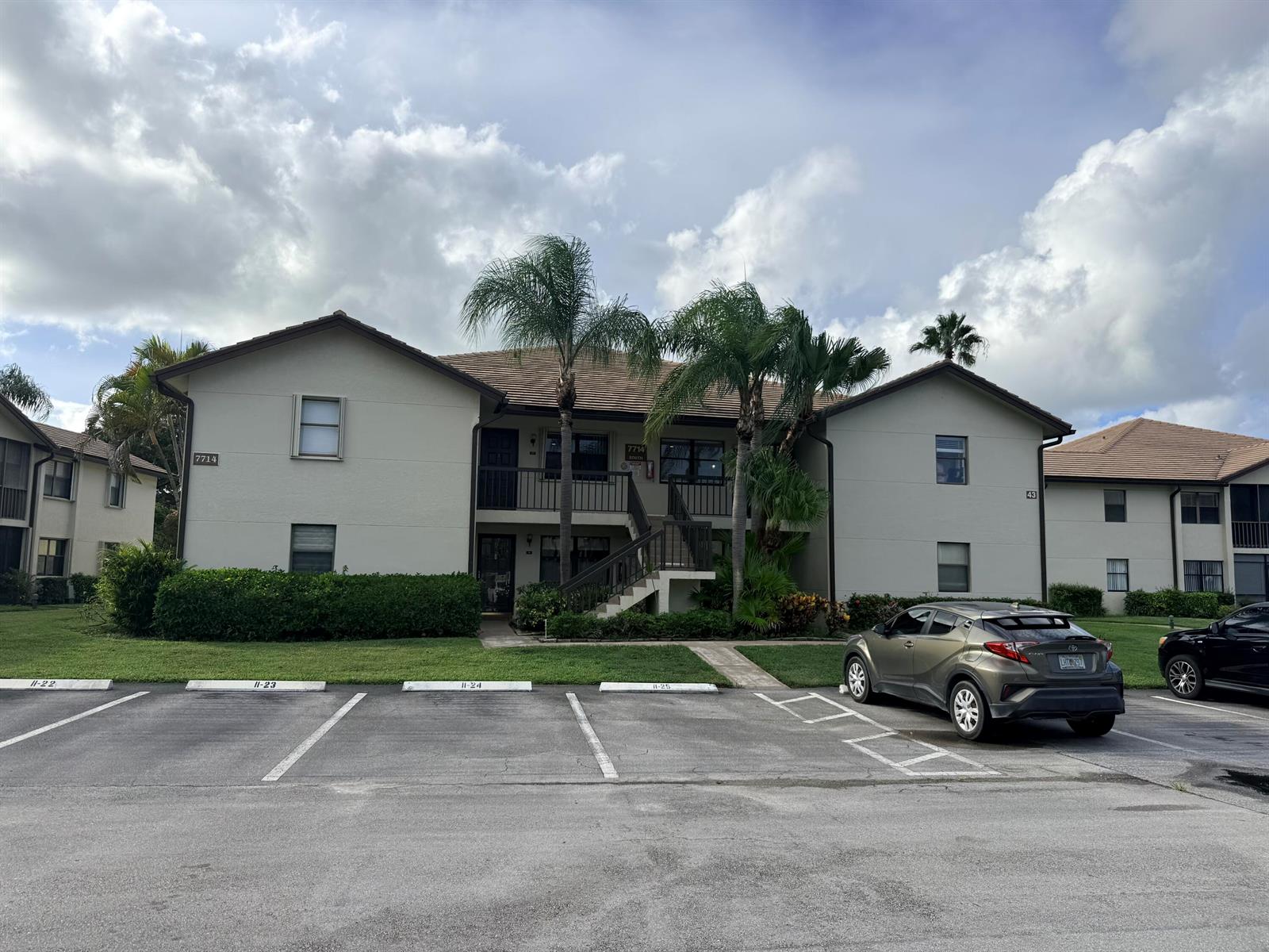 A two-story apartment building with a parking lot in the foreground and palm trees — 7714 Tahiti Lane # 203, FL 33467, FL