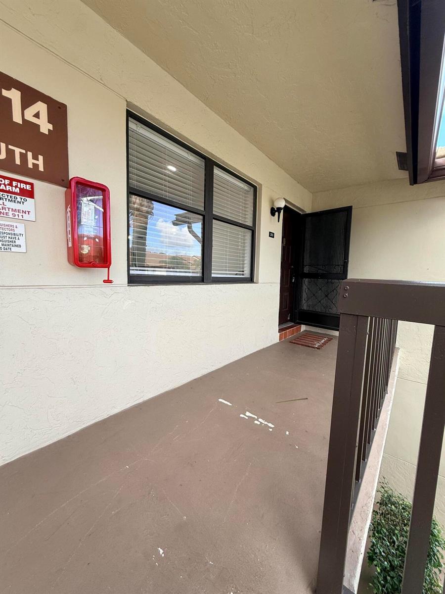 An exterior view of a covered apartment balcony with a red fire extinguisher cabinet — 7714 Tahiti Lane # 203, FL 33467, FL