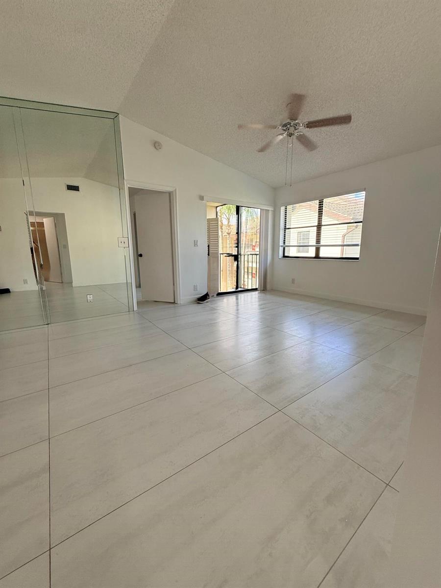 An empty room features large white floor tiles, a ceiling fan, and mirrored closet doors — 7714 Tahiti Lane # 203, FL 33467, FL