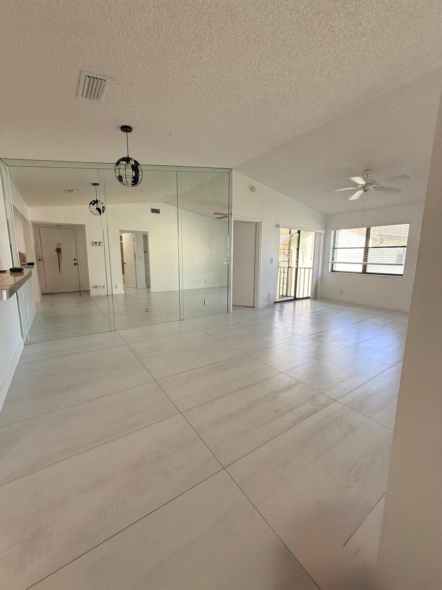 A living room with large white floor tiles, a mirrored wall, and a ceiling fan — 7714 Tahiti Lane # 203, FL 33467, FL