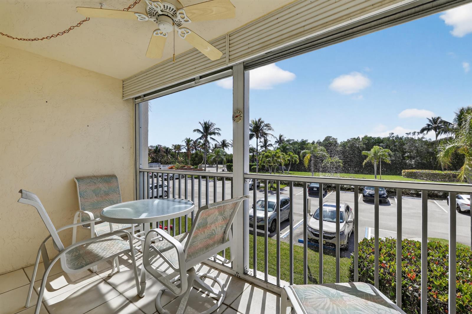 A screened-in balcony features a small table, chairs, a ceiling fan, and a parking view — 4444 NE Ocean Boulevard # 108, Jensen Beach FL 34957, JENSEN BEACH, FL