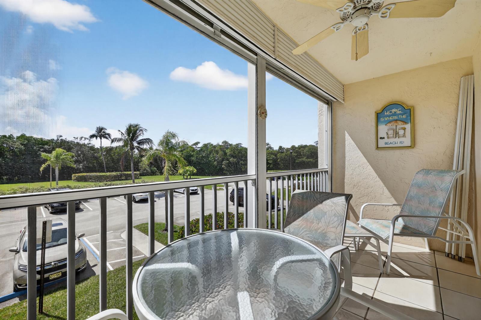 A screened-in balcony features a glass-topped table, two chairs, a ceiling fan, and parking views — 4444 NE Ocean Boulevard # 108, Jensen Beach FL 34957, JENSEN BEACH, FL
