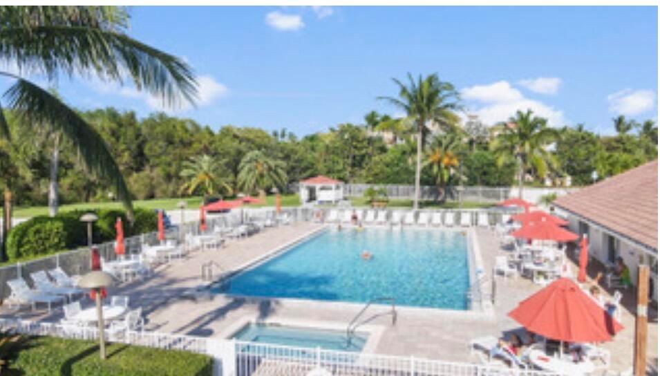 An outdoor swimming pool with a hot tub, lounge chairs, and red umbrellas — 4444 NE Ocean Boulevard # 108, Jensen Beach FL 34957, JENSEN BEACH, FL