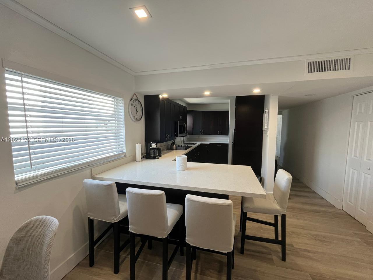 A kitchen features dark cabinets, white countertops, a breakfast bar with chairs, and light flooring — 6965 Harding Ave # 401, Miami Beach FL 33141, MIAMI BEACH, FL