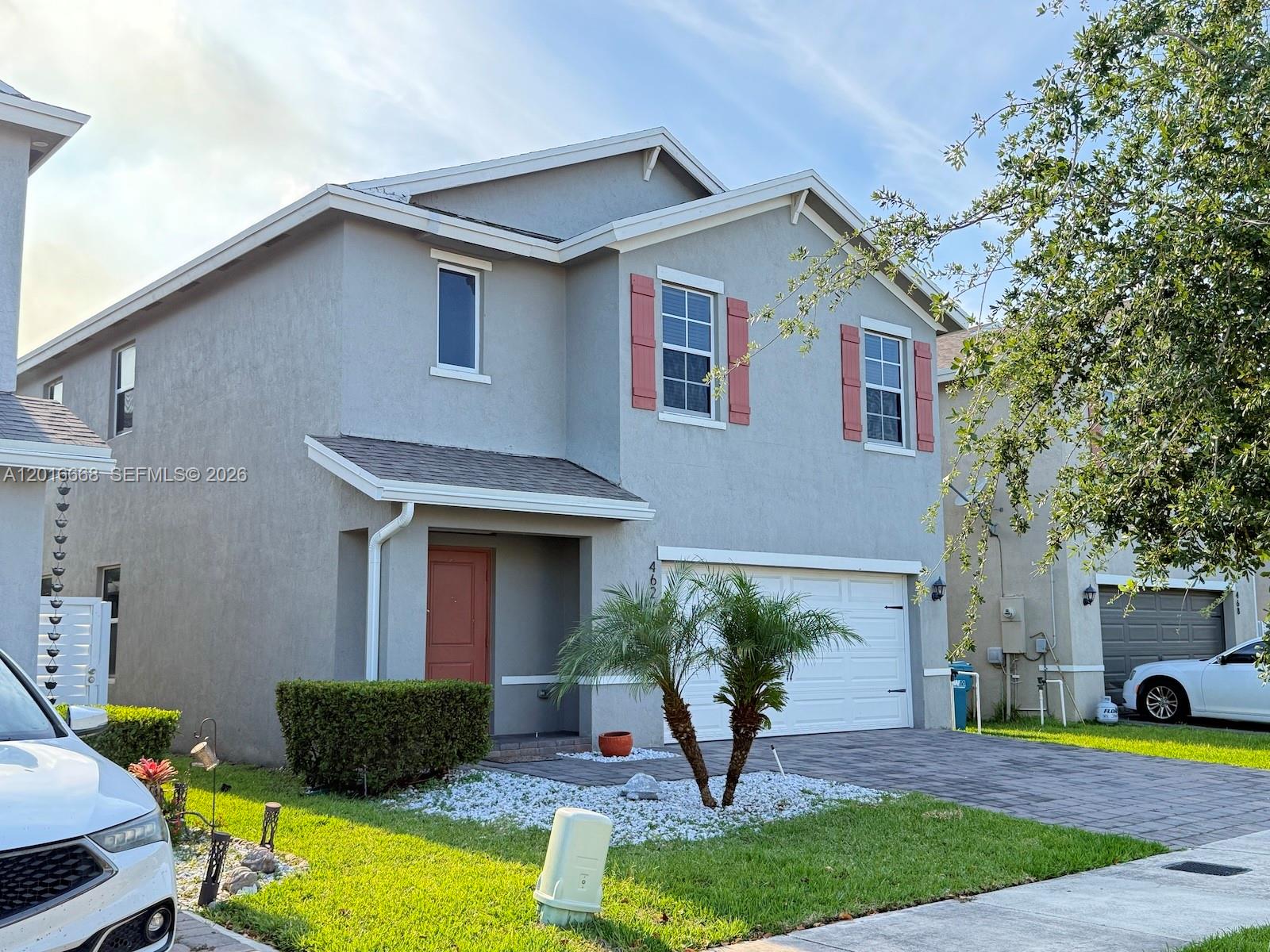 A two-story gray house features a white garage door, red shutters, and a paved driveway — 462 NE 6th Pl, Florida City FL 33034, FLORIDA CITY, FL