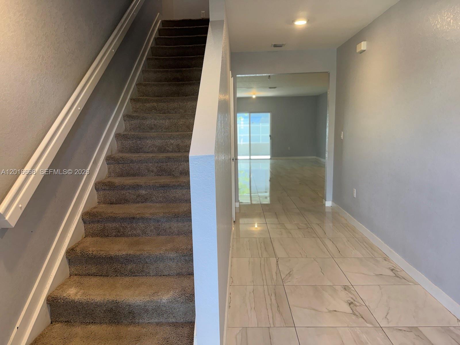 A carpeted staircase sits beside a tiled hallway leading to an open living area — 462 NE 6th Pl, Florida City FL 33034, FLORIDA CITY, FL