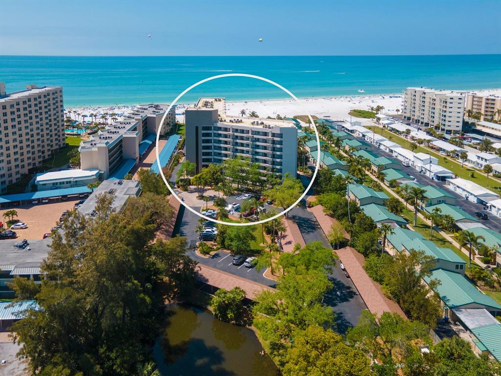 An aerial view shows a multi-story beachfront condominium building surrounded by parking and tropical landscaping — 5880 MIDNIGHT PASS ROAD UNIT 906, SARASOTA, FL