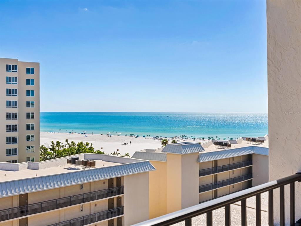 An elevated view of a sandy beach and ocean from a balcony with nearby buildings — 5880 MIDNIGHT PASS ROAD UNIT 906, SARASOTA, FL