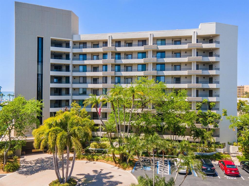 A multi-story beige apartment building with balconies, palm trees, and a parking lot in front — 5880 MIDNIGHT PASS ROAD UNIT 906, SARASOTA, FL