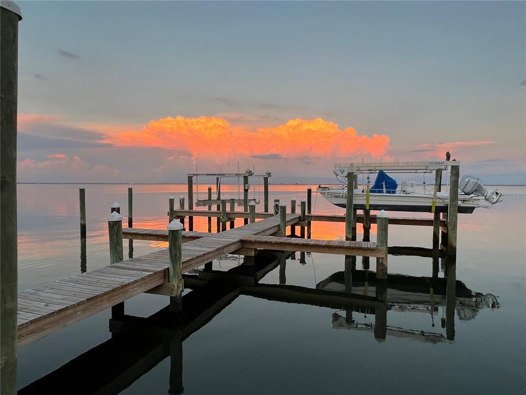 A wooden dock extends into calm water with a boat lift and sunset clouds above — 413 S BAYSHORE BOULEVARD UNIT 4, SAFETY HARBOR, FL