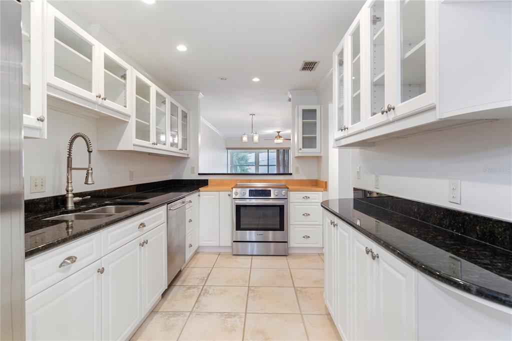 A galley kitchen features white cabinets, black granite countertops, stainless steel appliances, and tile flooring — 413 S BAYSHORE BOULEVARD UNIT 4, SAFETY HARBOR, FL