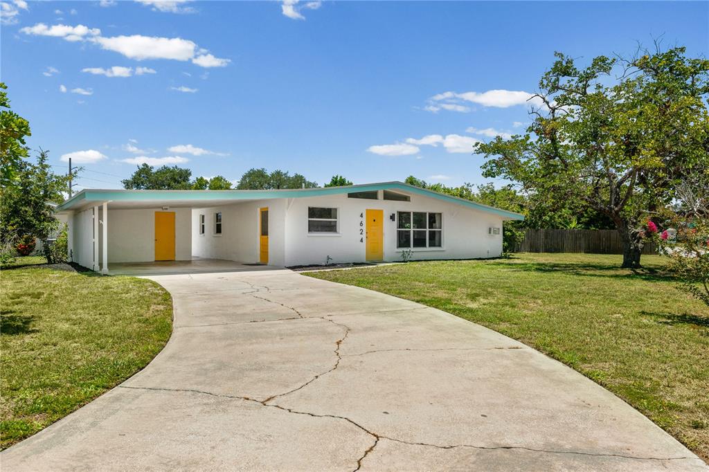 A white single-story house with a carport and yellow doors sits on a grassy lot — 4624 NAOMI RIDGE LANE, SARASOTA, FL