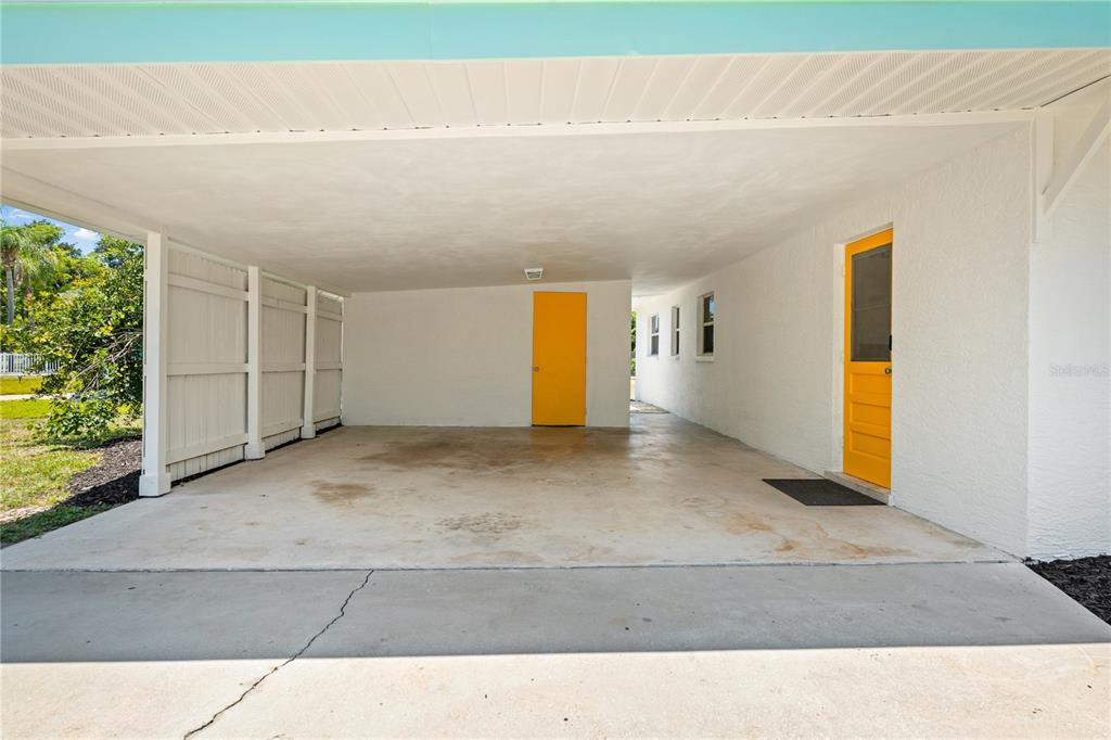 A concrete carport features white walls, a light blue trim, and two bright yellow doors — 4624 NAOMI RIDGE LANE, SARASOTA, FL