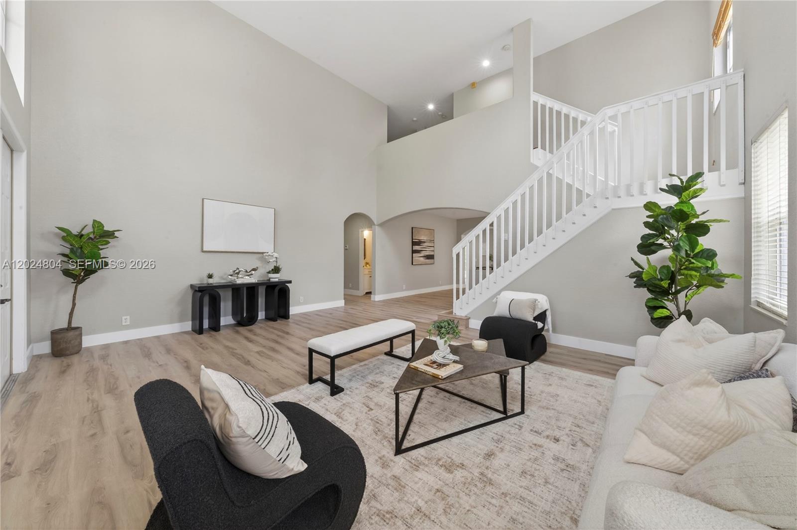 A bright living room features high ceilings, a staircase with white railings, and modern furniture — 2432 Deer Creek Rd, Weston FL 33327, WESTON, FL