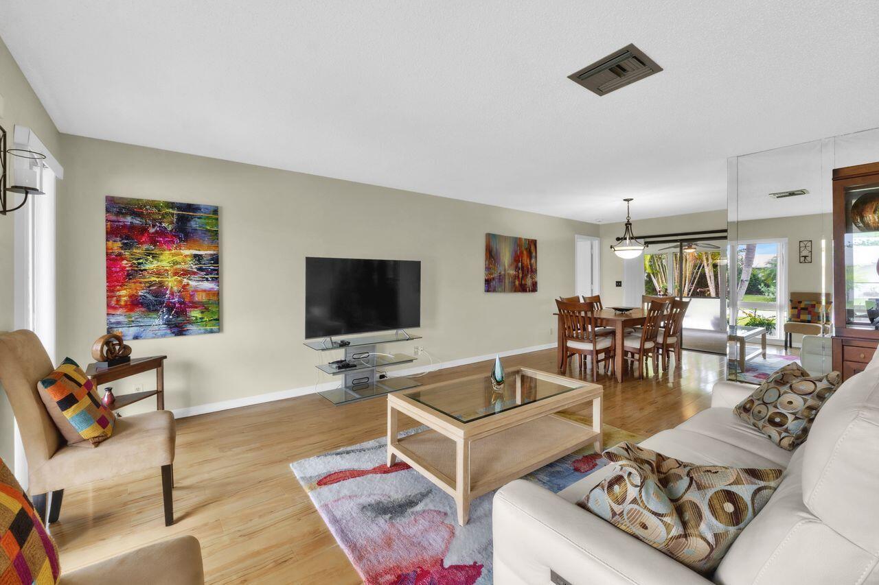 A living room with light wood floors, a glass coffee table, and colorful abstract art — 14765 Country Lane, Delray Beach FL 33484, DELRAY BEACH, FL