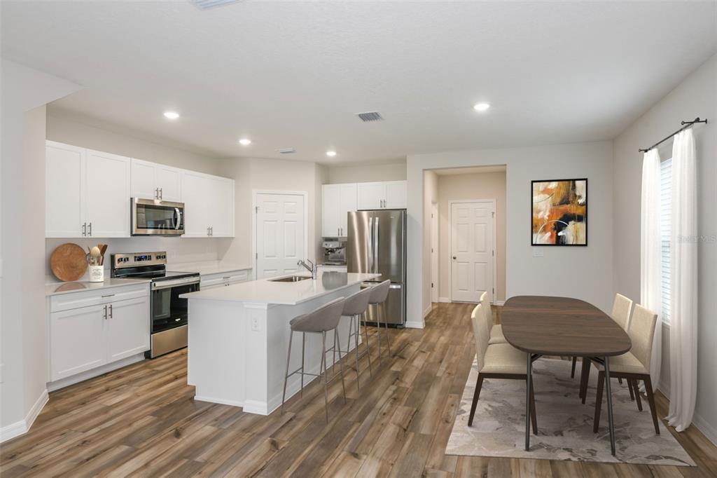 A modern kitchen features white cabinets, a central island with bar seating, and an adjacent dining area — 9888 PELICAN COAST DRIVE, DADE CITY, FL