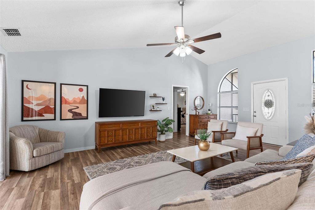 A living room features a vaulted ceiling, wood-look flooring, a television, and a ceiling fan — 7542 GUNSTOCK DRIVE, LAKELAND, FL