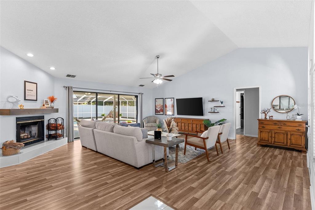 A living room features wood-look flooring, a fireplace, a vaulted ceiling, and sliding glass doors — 7542 GUNSTOCK DRIVE, LAKELAND, FL