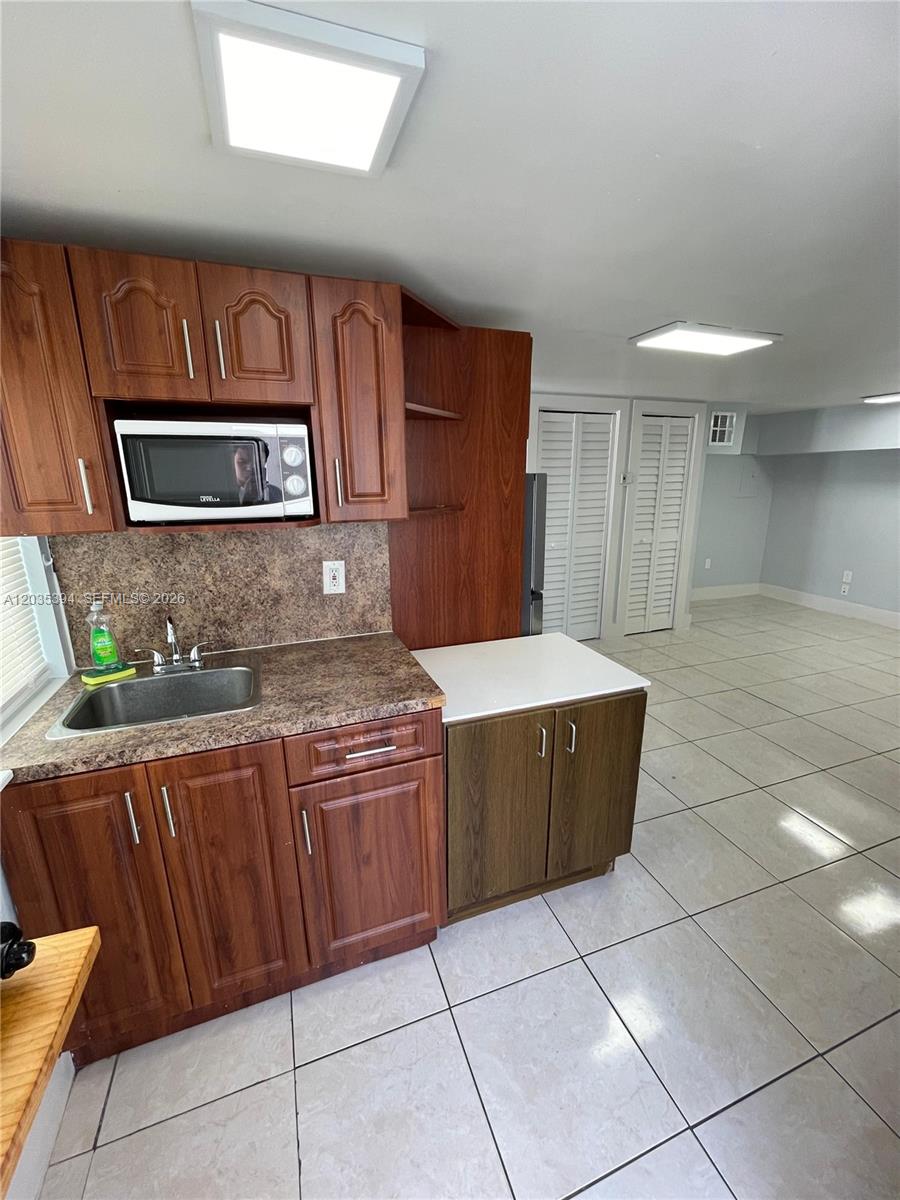 A small kitchen features wood cabinets, a stainless steel sink, and light-colored floor tiles — 3333 W 4th Ave # A, Hialeah FL 33012, HIALEAH, FL