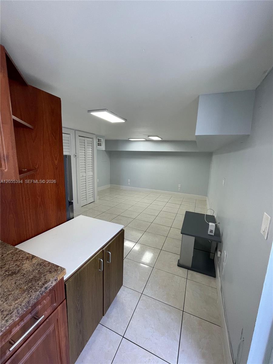 A kitchen area with wood cabinets and tile flooring opens into a large, empty room — 3333 W 4th Ave # A, Hialeah FL 33012, HIALEAH, FL