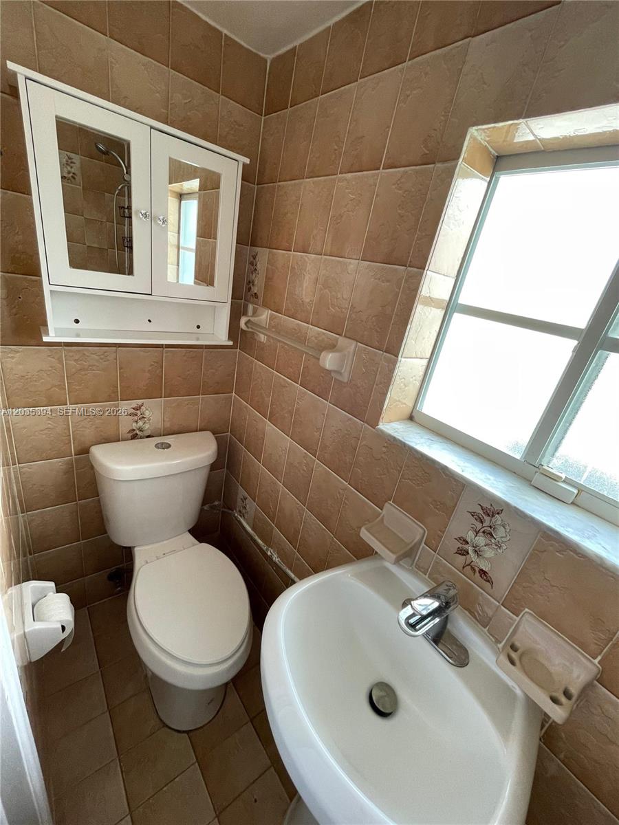 A small bathroom features tan wall tiles, a white toilet, a pedestal sink, and a cabinet — 3333 W 4th Ave # A, Hialeah FL 33012, HIALEAH, FL