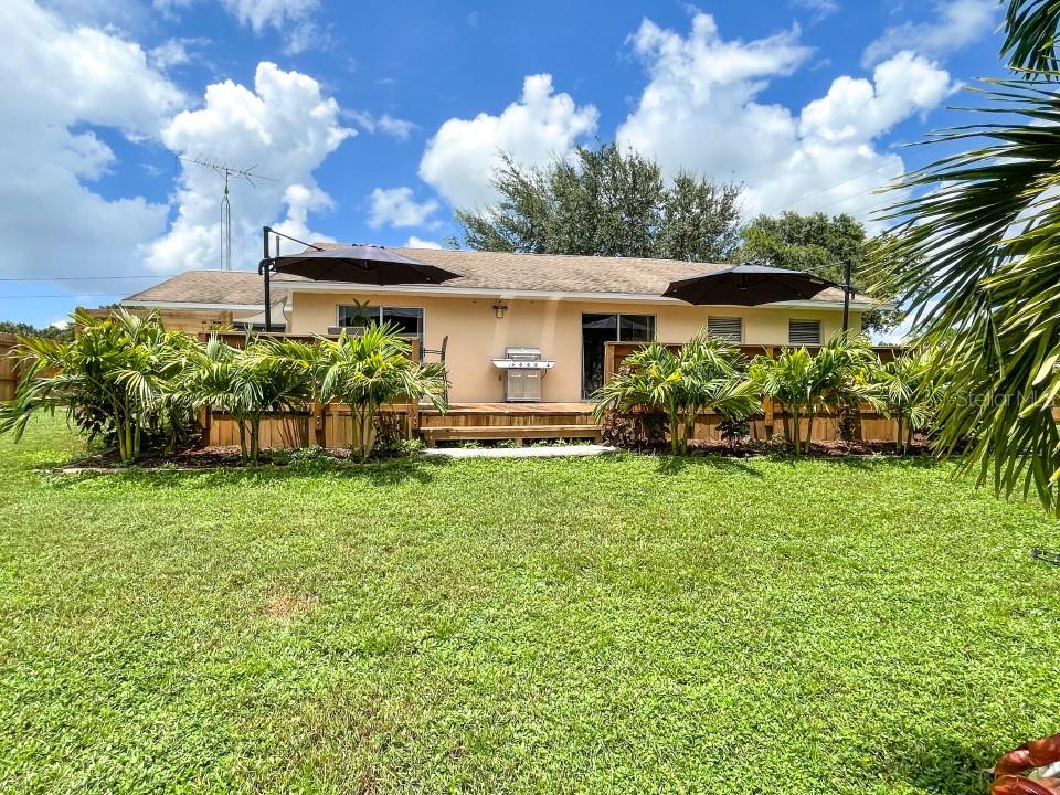 A tan house exterior features a wooden deck with two umbrellas and a stainless grill — 100 DREAMTIME AVENUE, LAKE PLACID, FL