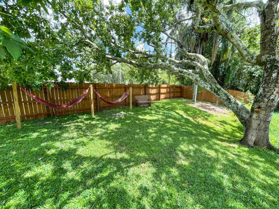 A grassy backyard features a wooden fence, two red hammocks, and a small wooden bench — 100 DREAMTIME AVENUE, LAKE PLACID, FL