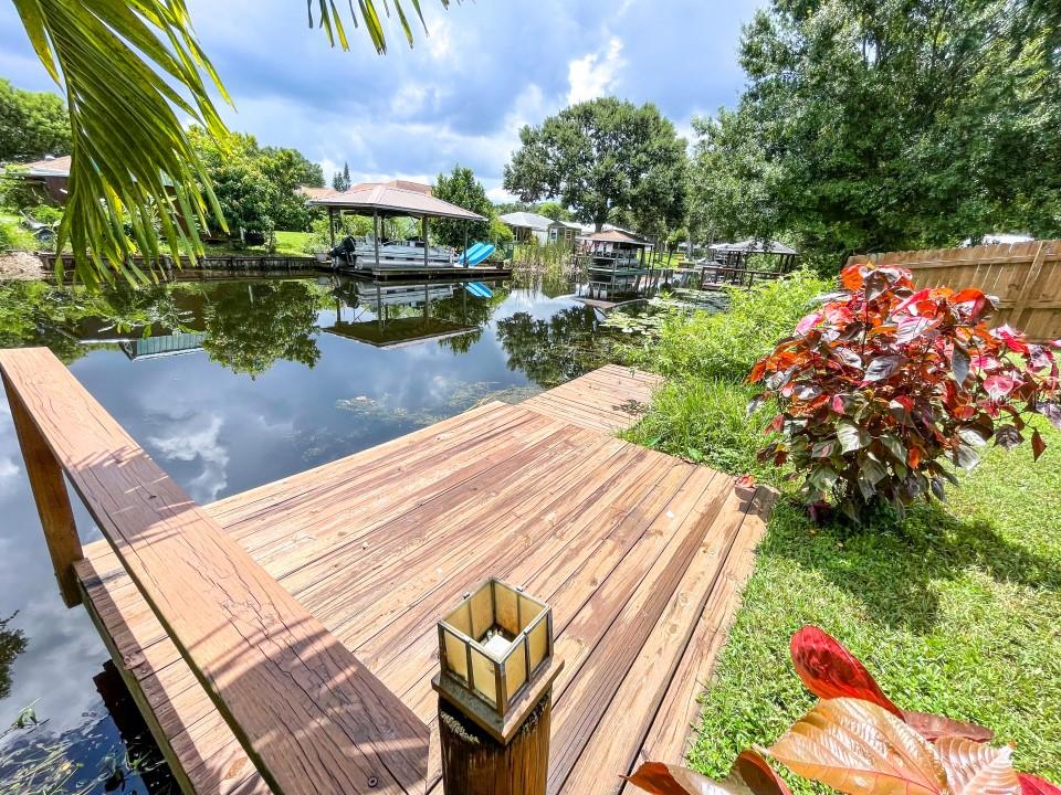 A wooden deck overlooks a calm canal with boat docks and lush green trees — 100 DREAMTIME AVENUE, LAKE PLACID, FL