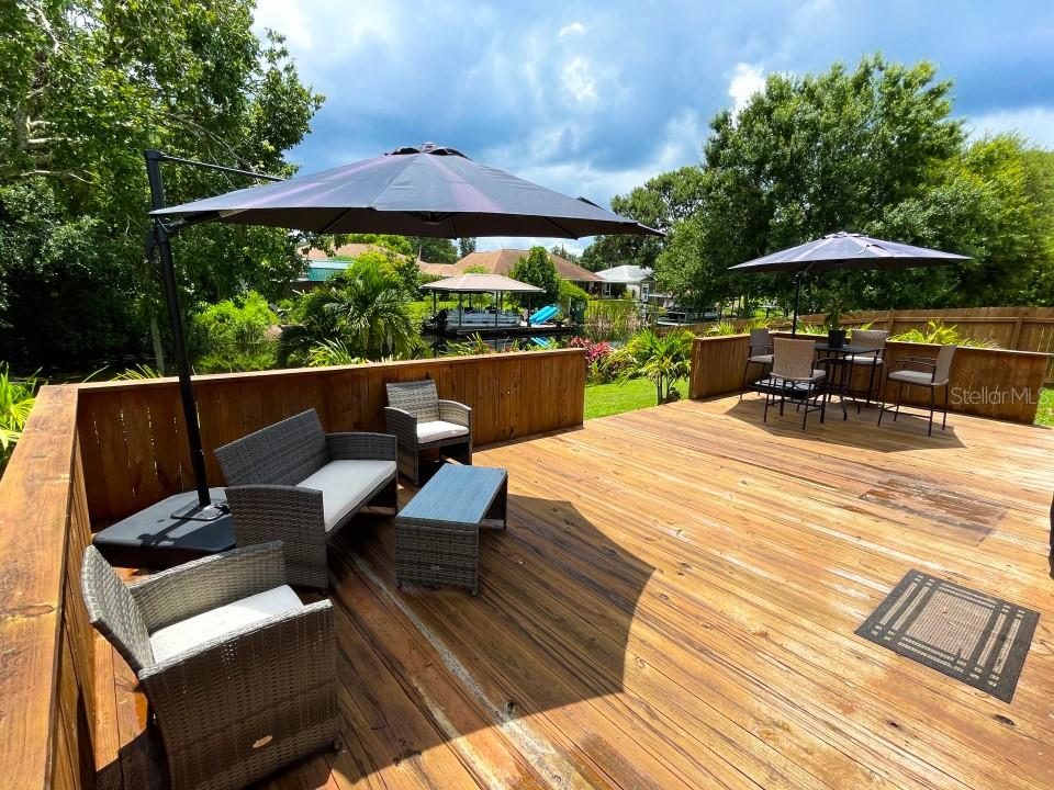 A wooden deck features outdoor furniture, two umbrellas, and a view of a canal — 100 DREAMTIME AVENUE, LAKE PLACID, FL
