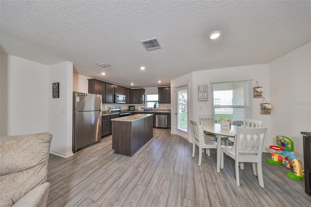 A kitchen with dark cabinets, granite countertops, and a dining area with white chairs — 5311 NEW FRIENDSHIP PLACE, TAMPA, FL