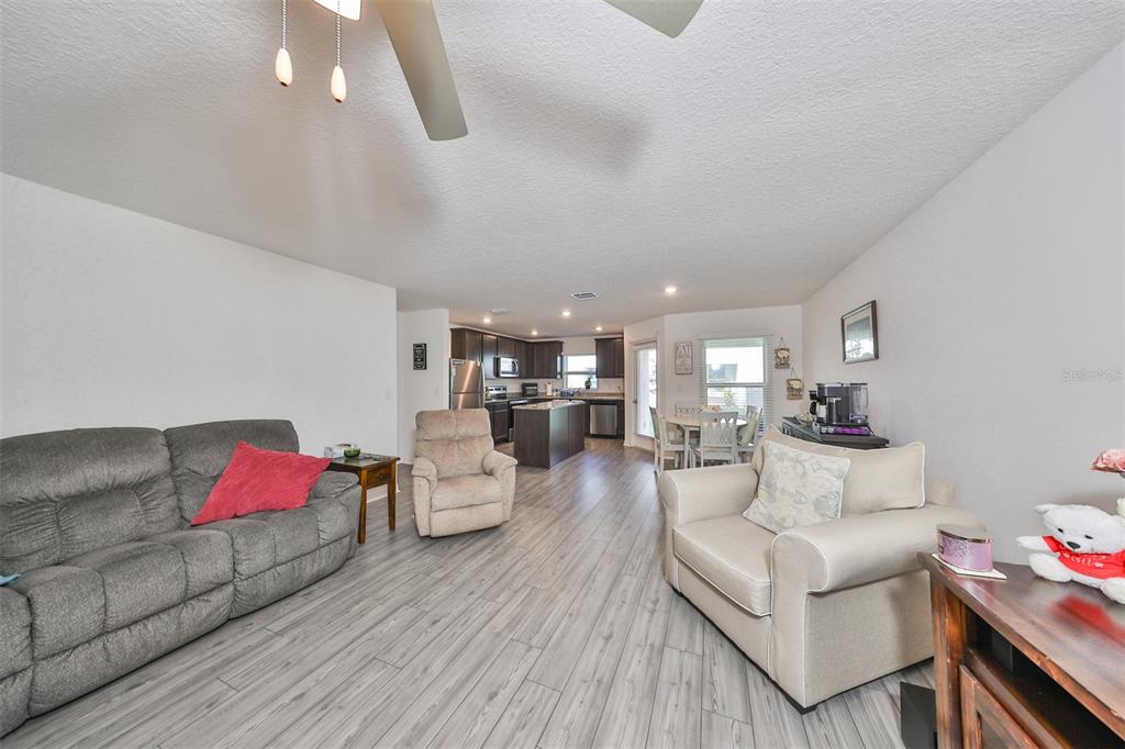 An open-concept living room features wood-look flooring, a ceiling fan, and an adjacent kitchen — 5311 NEW FRIENDSHIP PLACE, TAMPA, FL