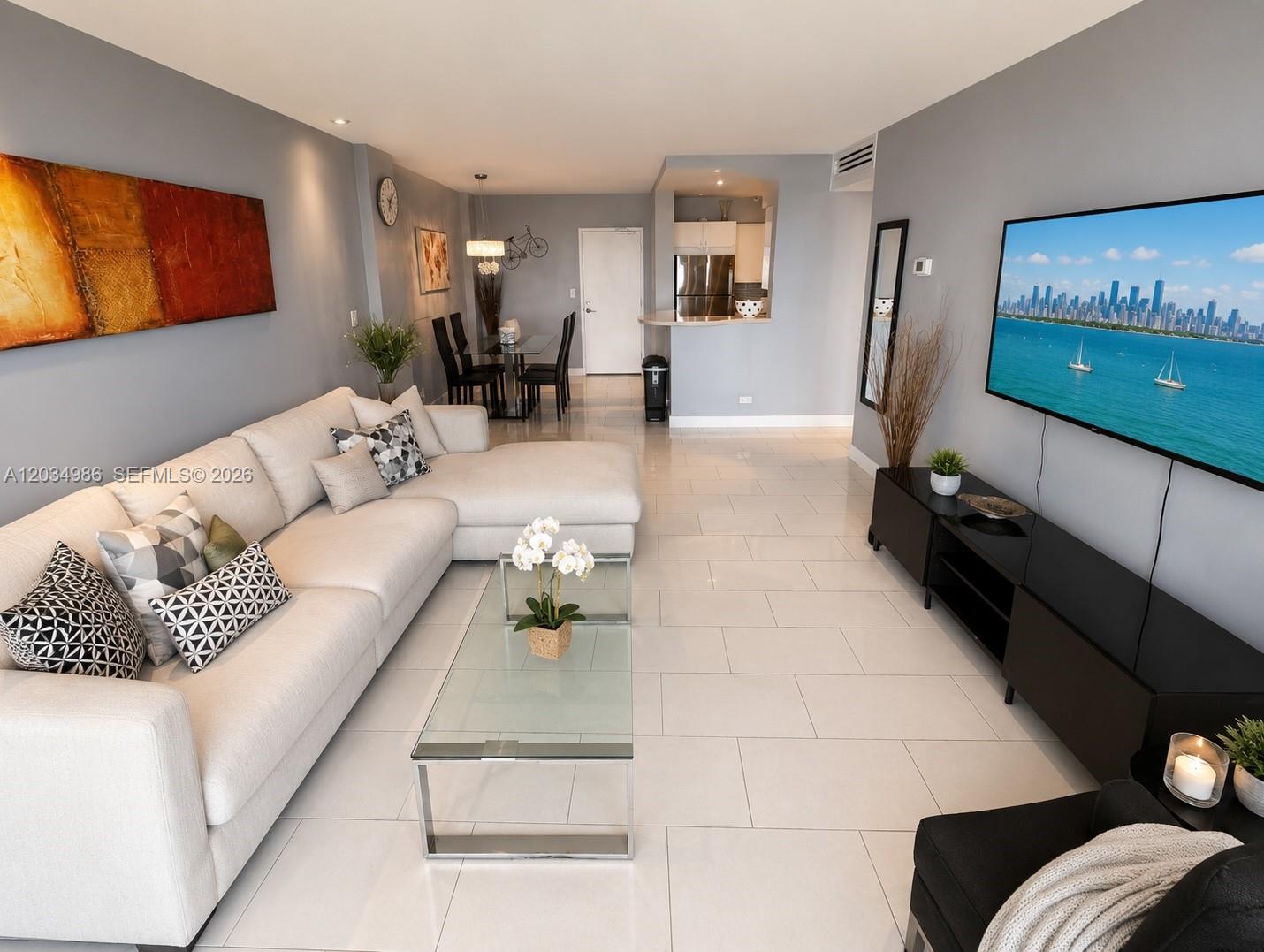 A living room features a sectional sofa, glass coffee table, and wall-mounted television on tile floors — MIAMI BEACH, FL