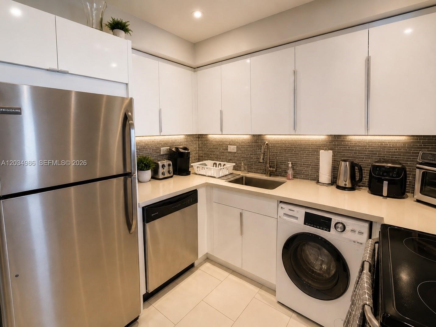A kitchen features white cabinets, stainless steel appliances, a built-in washer, and gray tile backsplash — MIAMI BEACH, FL