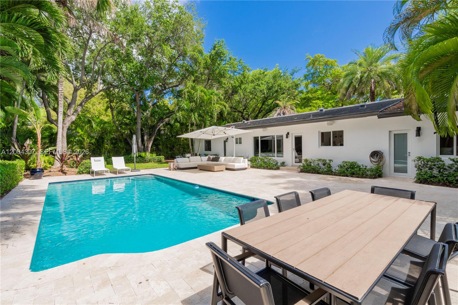 A backyard features a swimming pool, a patio with outdoor furniture, and lush green trees — 1029 Mariposa Ave, Coral Gables FL 33146, CORAL GABLES, FL