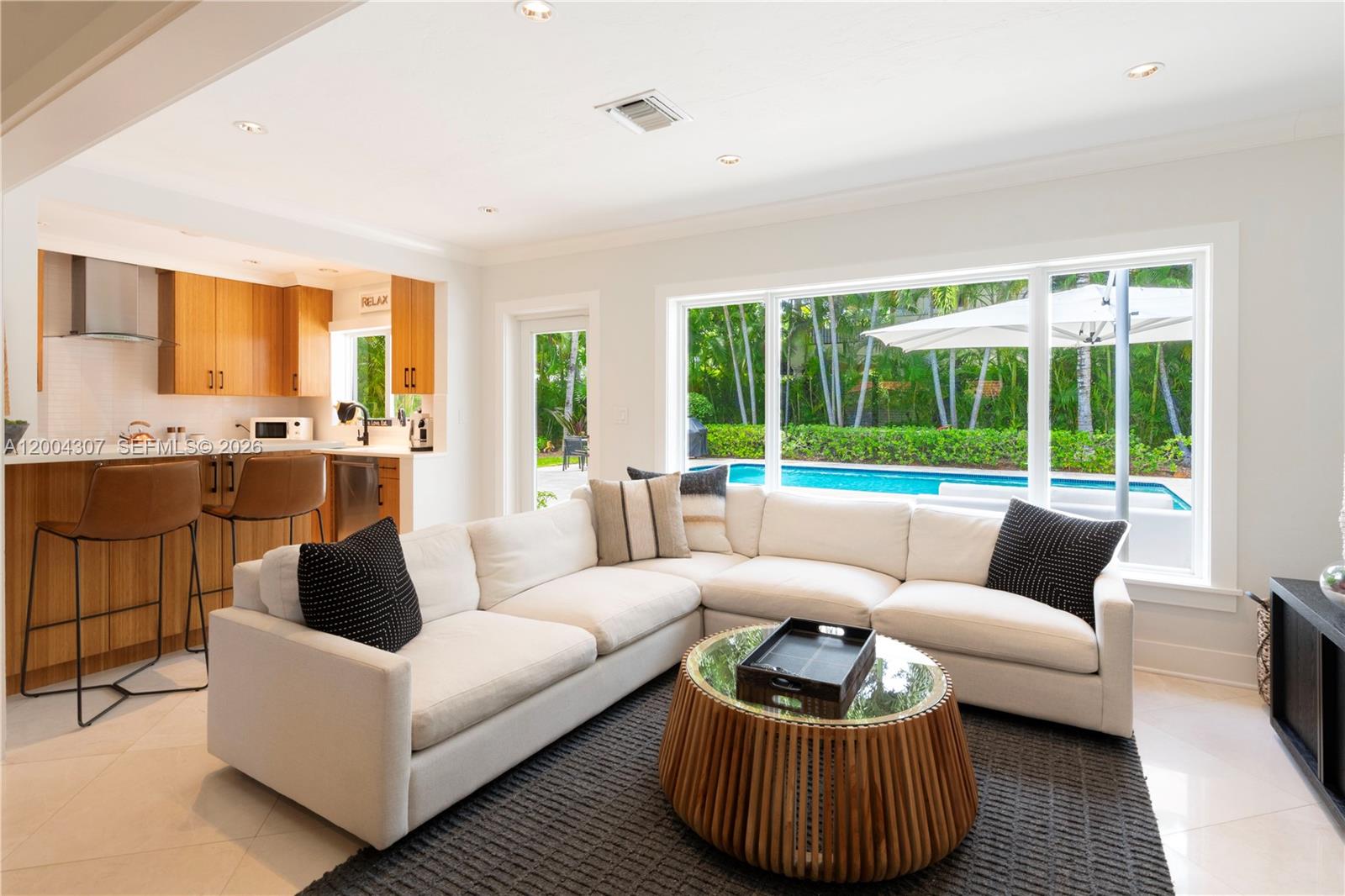 A living room with a white sectional sofa, round coffee table, and view of a pool — 1029 Mariposa Ave, Coral Gables FL 33146, CORAL GABLES, FL