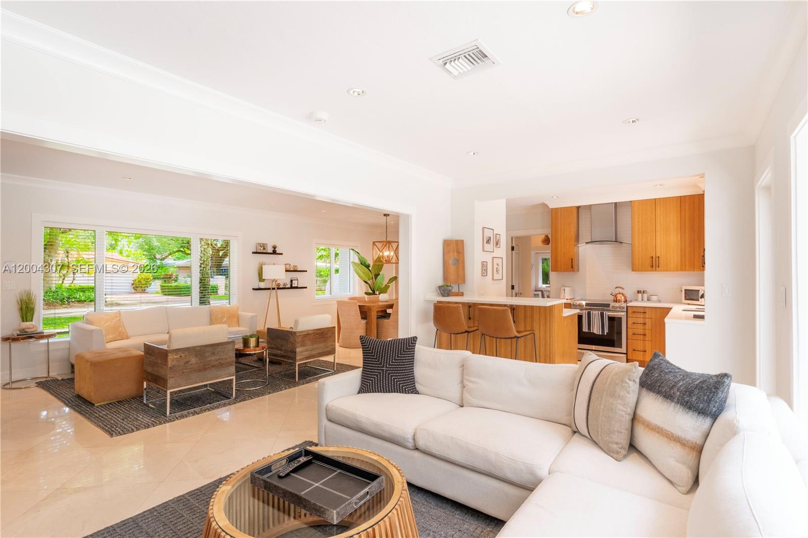 A bright, open-concept living room and kitchen featuring light wood cabinetry and white sofas — 1029 Mariposa Ave, Coral Gables FL 33146, CORAL GABLES, FL