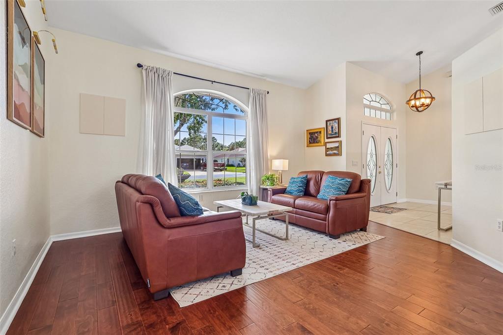 A living room with wood floors, two brown leather sofas, and a large arched window — 64 LAKE DIAMOND BOULEVARD, OCALA, FL