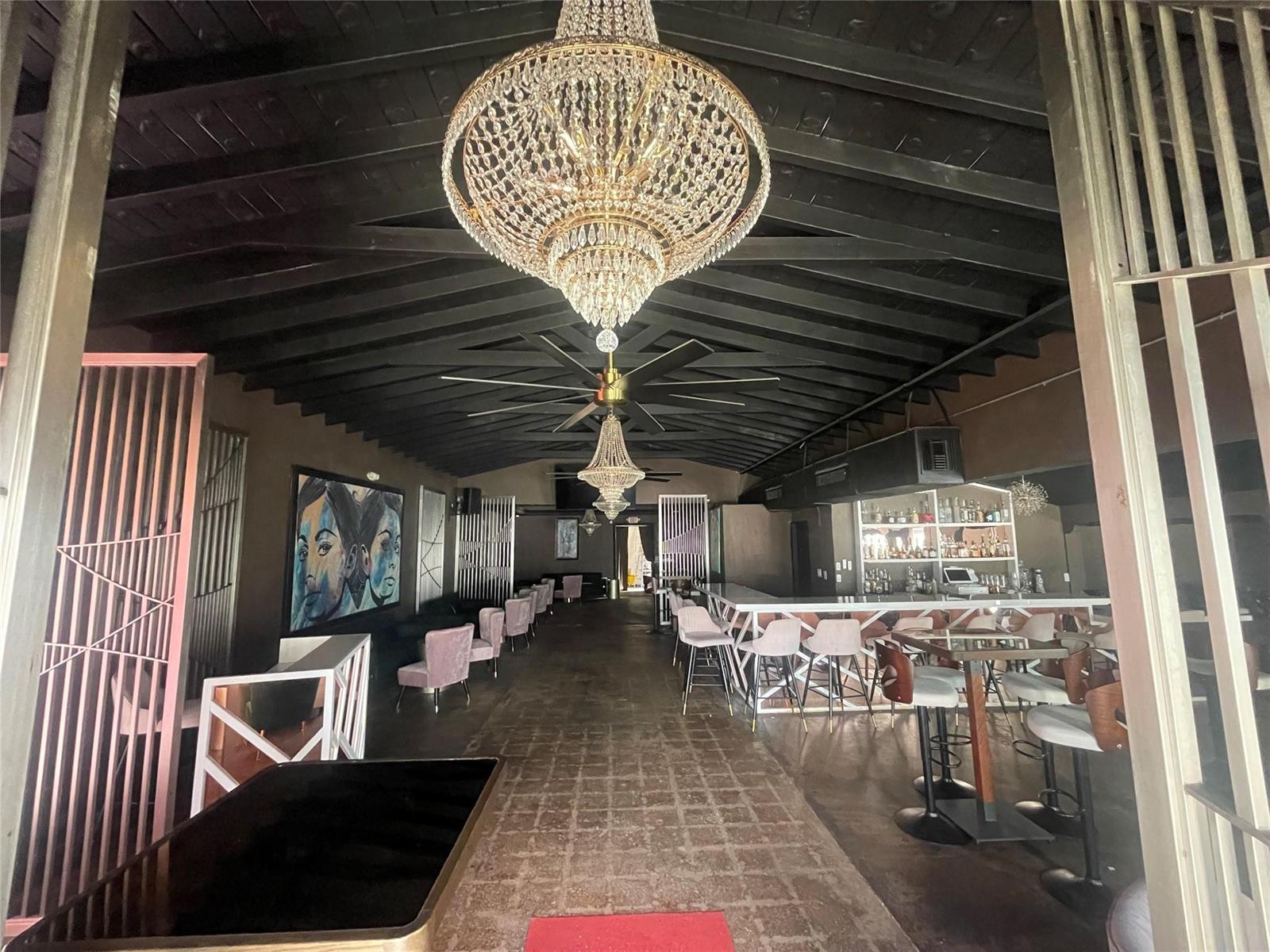 A bar interior features a dark vaulted ceiling, crystal chandeliers, and a long service counter — FORT LAUDERDALE, FL