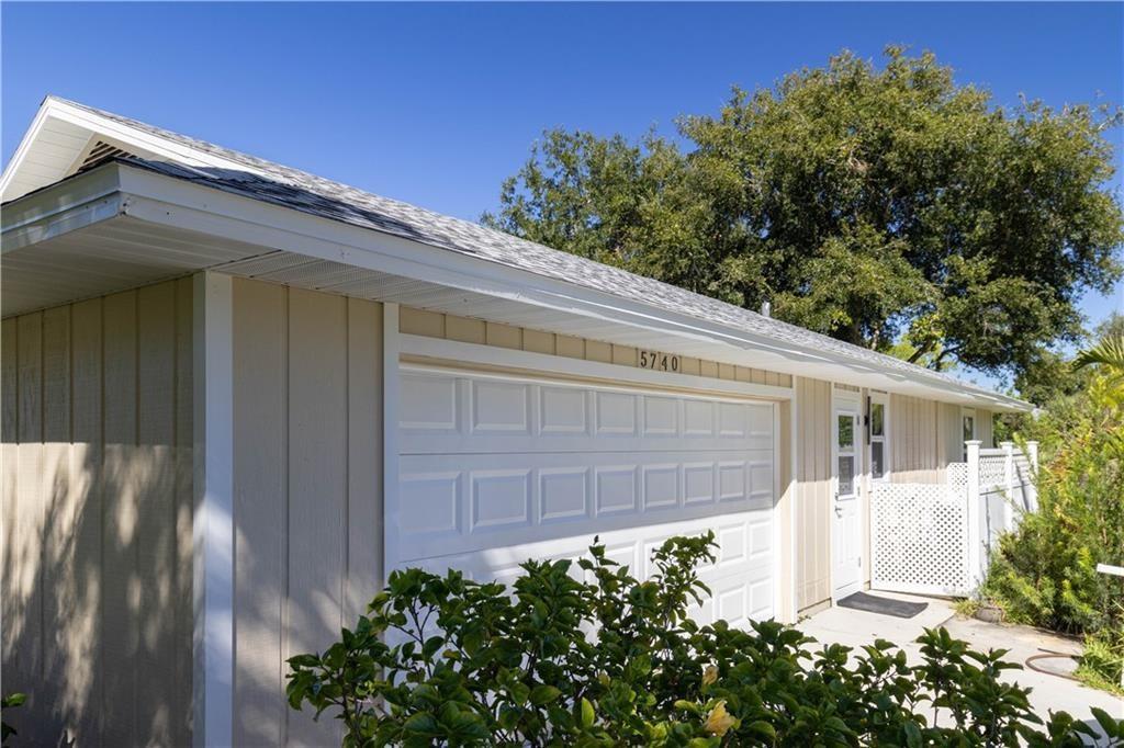 A tan house exterior features a white garage door, a side door, and a shingled roof — 5740 36th Place, Vero Beach FL 32966, VERO BEACH, FL