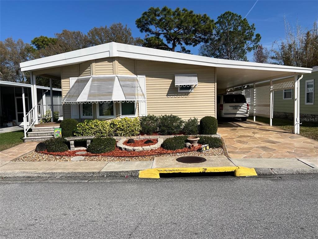 A single-story manufactured home with a tan exterior, a front bay window, and a carport — 1001 STARKEY ROAD UNIT 90, LARGO, FL