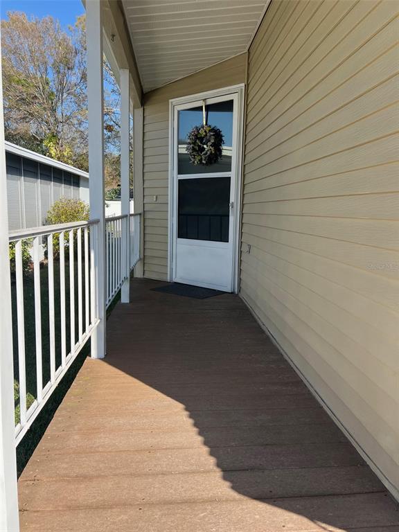 A covered wooden porch leads to a white storm door on a tan-sided home — 1001 STARKEY ROAD UNIT 90, LARGO, FL