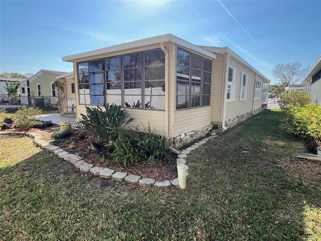 A beige mobile home with a screened-in porch and a stone-bordered garden bed — 1001 STARKEY ROAD UNIT 90, LARGO, FL