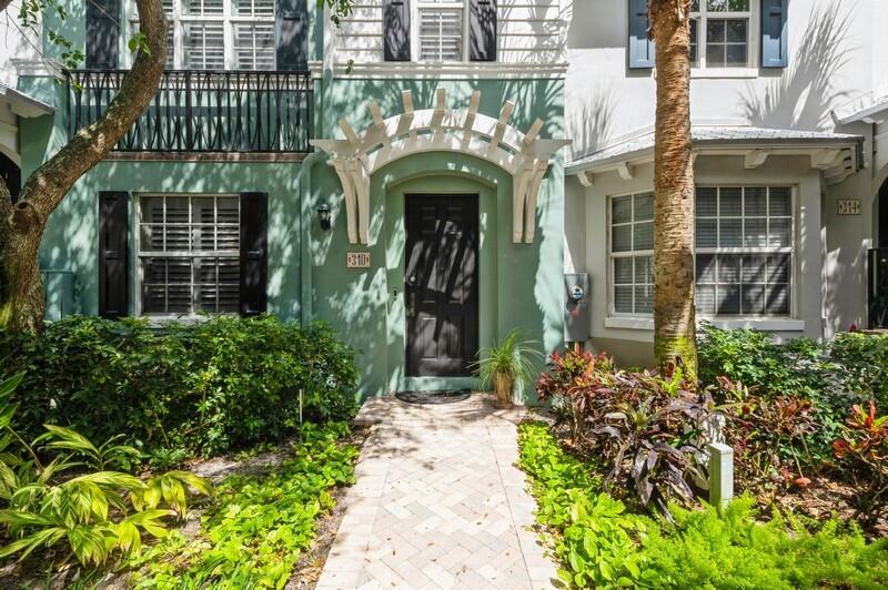 The exterior of a green townhouse features a black front door with a white pergola — 310 E Mallory Circle, Delray Beach FL 33483, DELRAY BEACH, FL