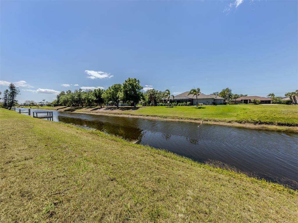 A grassy backyard slopes down to a canal with houses visible in the distance — 65 FAIRWAY ROAD, ROTONDA WEST, FL