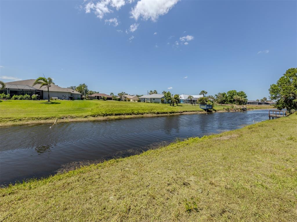 A grassy backyard slopes down to a canal with houses in the background — 65 FAIRWAY ROAD, ROTONDA WEST, FL